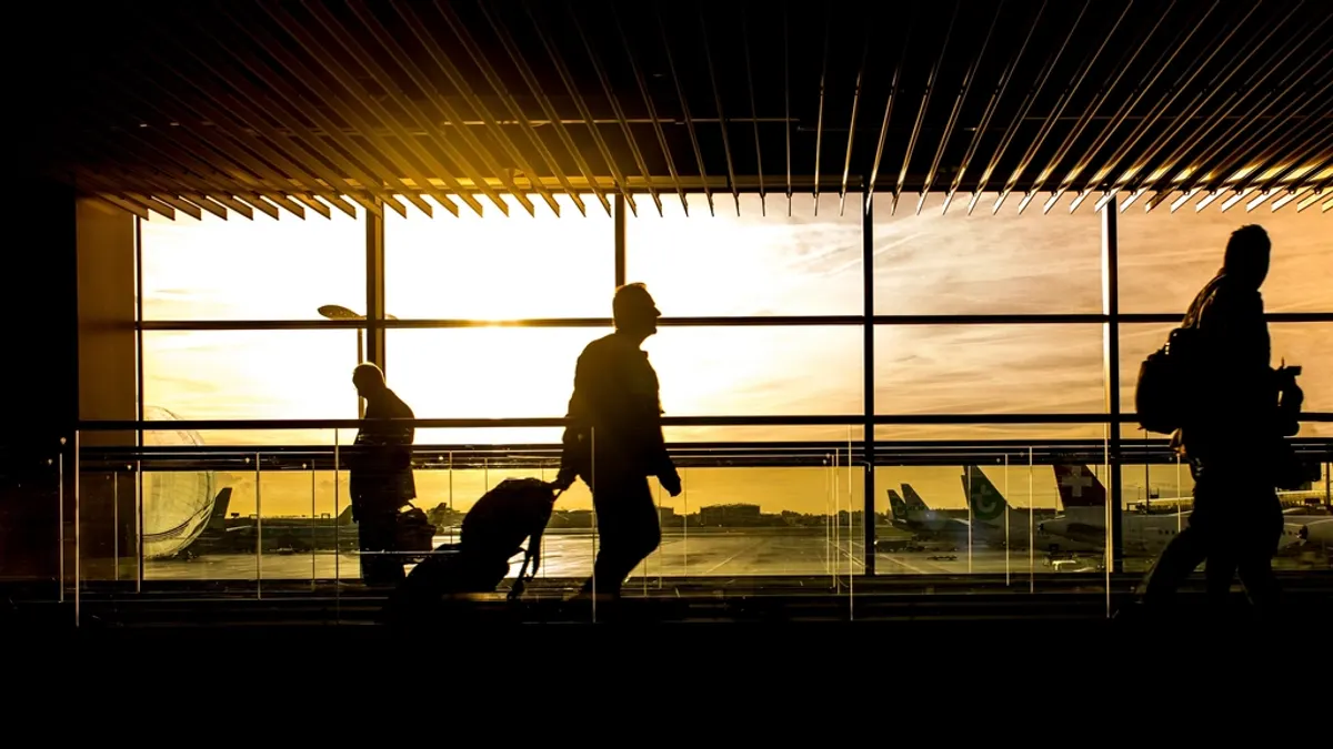 Voyageurs devant les baies vitrées d'un aéroport au coucher du soleil